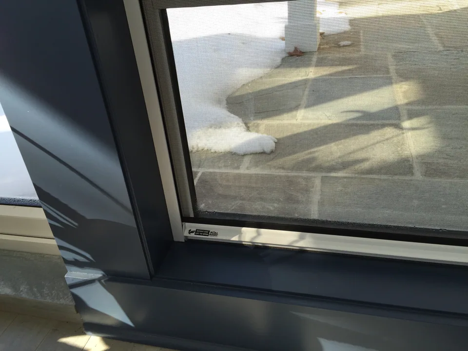 Retractable window screen fitted above a residential window, partially drawn down